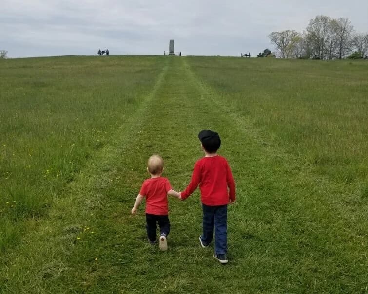 Two young visitors walking hand-in-hand toward a monument on the battlefield
